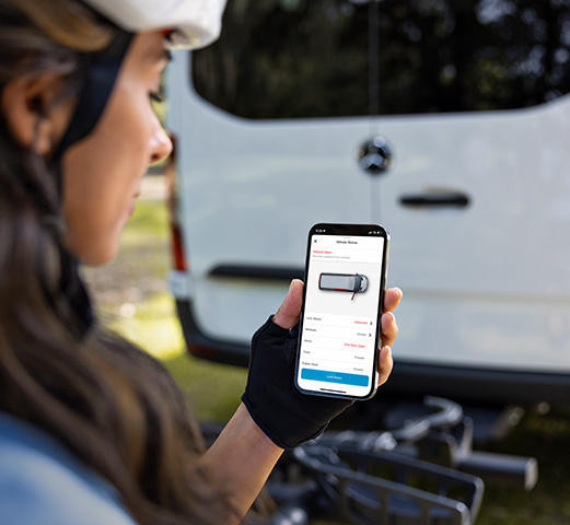 A person standing outdoors holding a phone and using the Mercedes me connect app for their Mercedes-Benz Adventure van. 